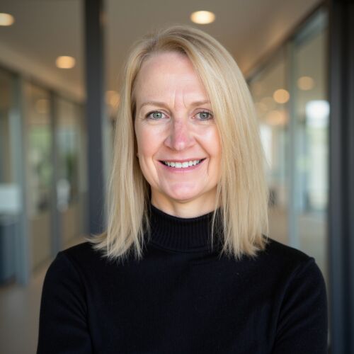 headshot of kathy kelly wearing a black turtleneck with an office visible in the background she's looking at the camera smiling