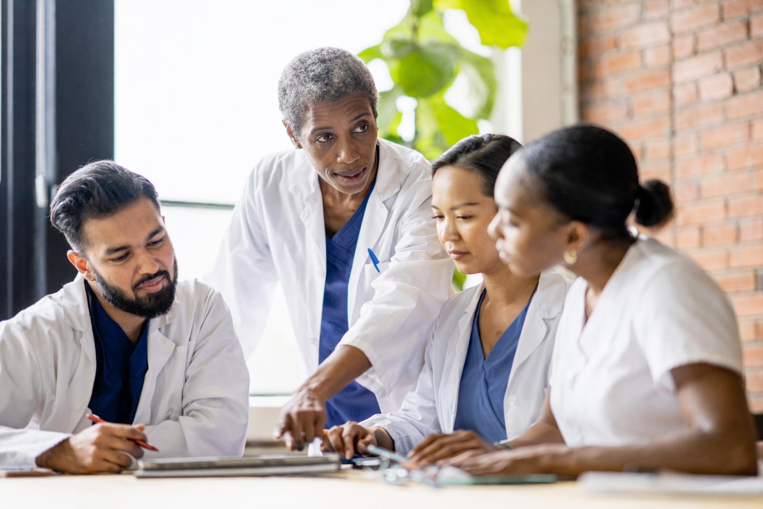 a diverse group of physicians gathered around a table looking at a tablet together